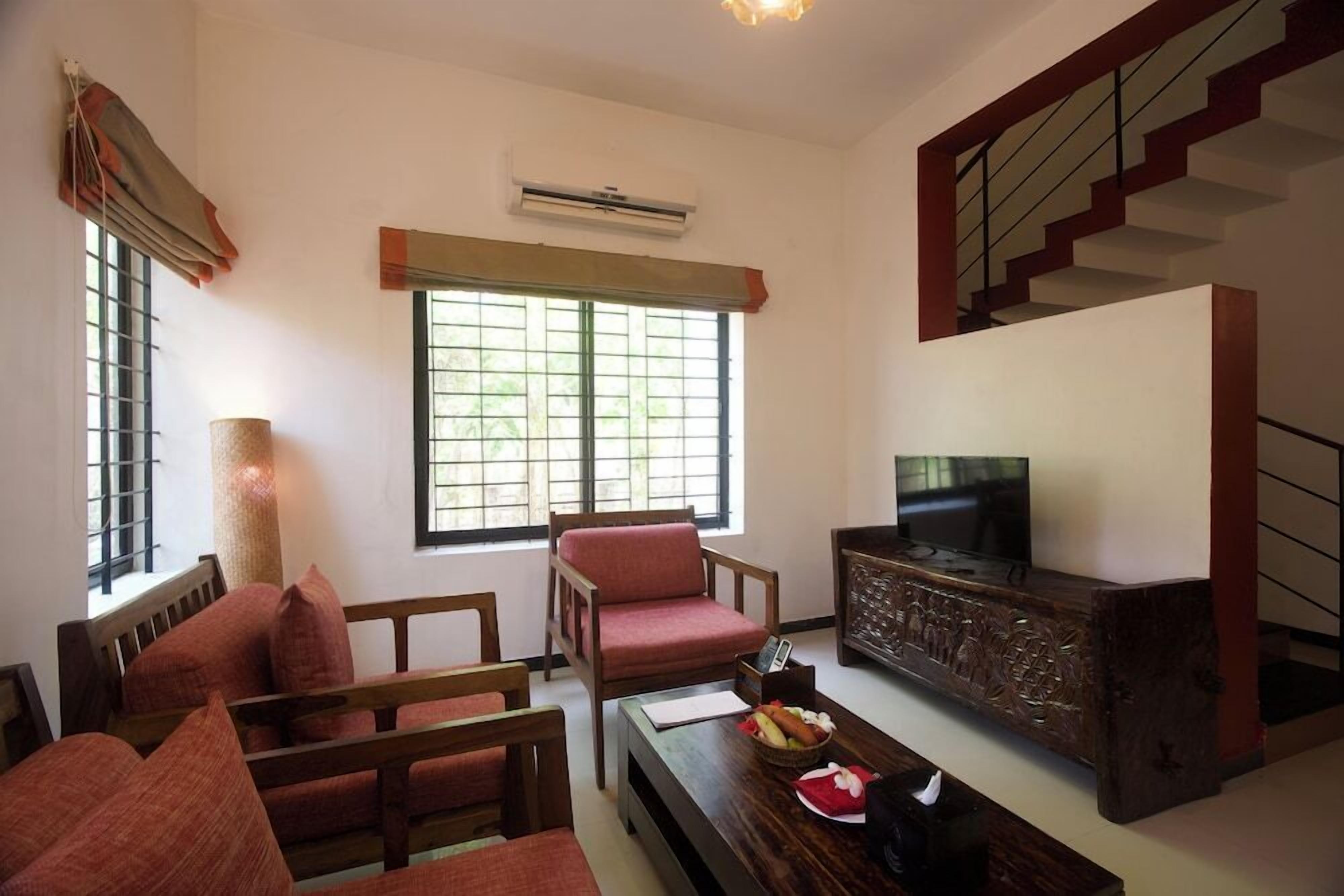A living room with a sofa, chairs, a coffee table, a television, and a staircase.
