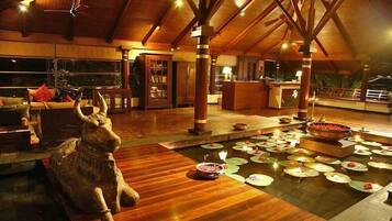 A spacious indoor area with a wooden ceiling, a reception desk, a seating area, and a decorative water feature with lotus leaves and candles.