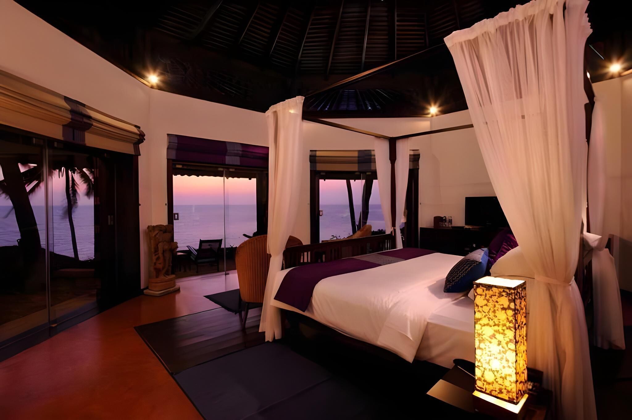 A bedroom with a large bed, a nightstand, a lamp, and a view of the ocean.