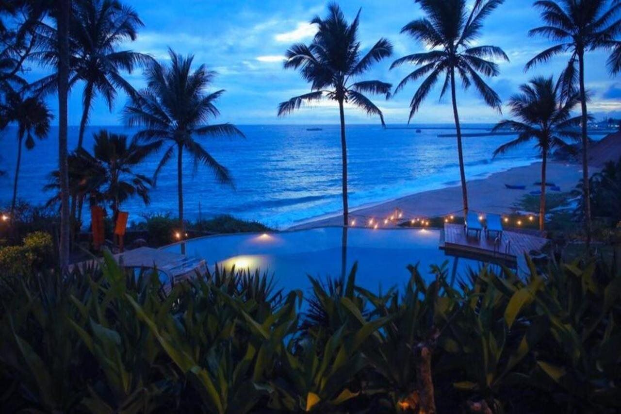 A poolside view with palm trees and a beach at dusk.
