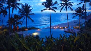 A poolside view with palm trees and a beach at dusk.