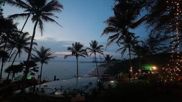 A beach scene with palm trees, a pool, and a view of the sea.