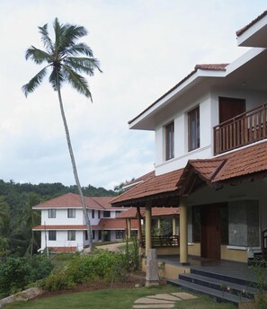 A two-story building with a balcony, surrounded by greenery and a palm tree. - Niraamaya Retreats Surya Samudra Kovalam (Neyyattinkara)