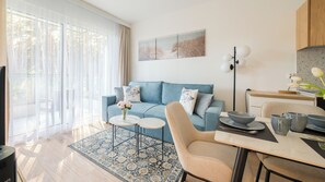 A modern living room with a blue sofa, a coffee table, and a dining area with a table and chairs. - Apartamenty Sun & Snow Plażowa V (Międzywodzie)