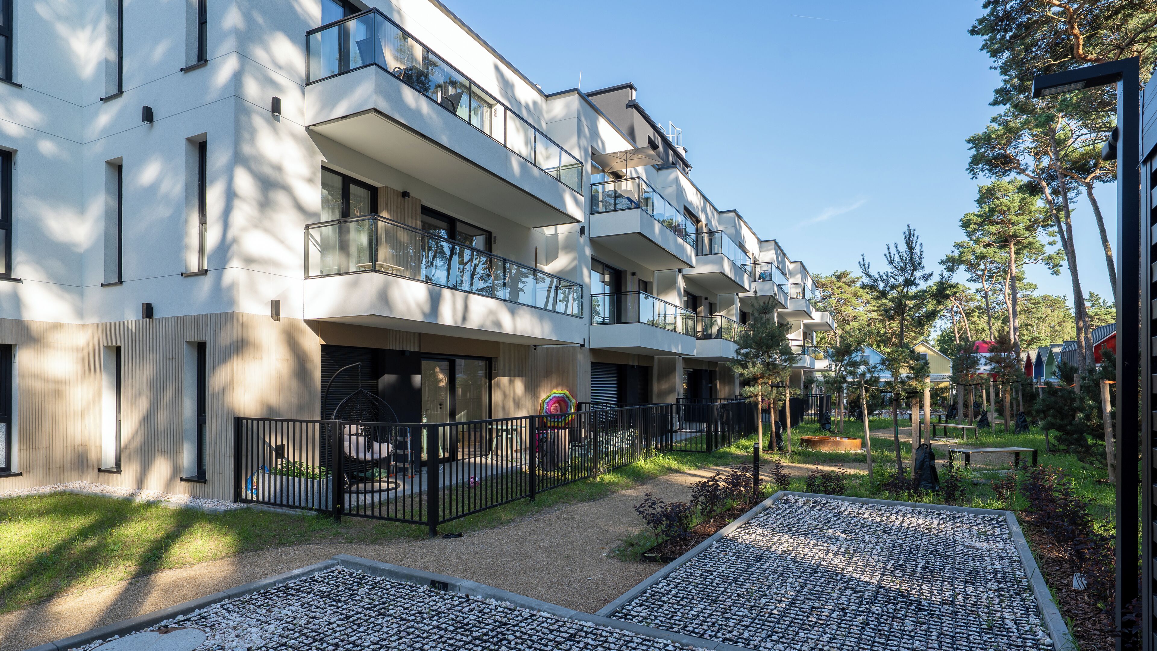 Un moderno edificio residencial de varios pisos con balcones, un patio empedrado y zonas verdes circundantes.