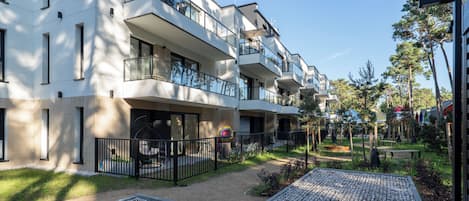 Un moderno edificio residencial de varios pisos con balcones, un patio empedrado y zonas verdes circundantes.