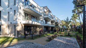 A modern multi-story residential building with balconies, a paved courtyard, and surrounding greenery. - Apartamenty Sun & Snow Plażowa V (Międzywodzie)