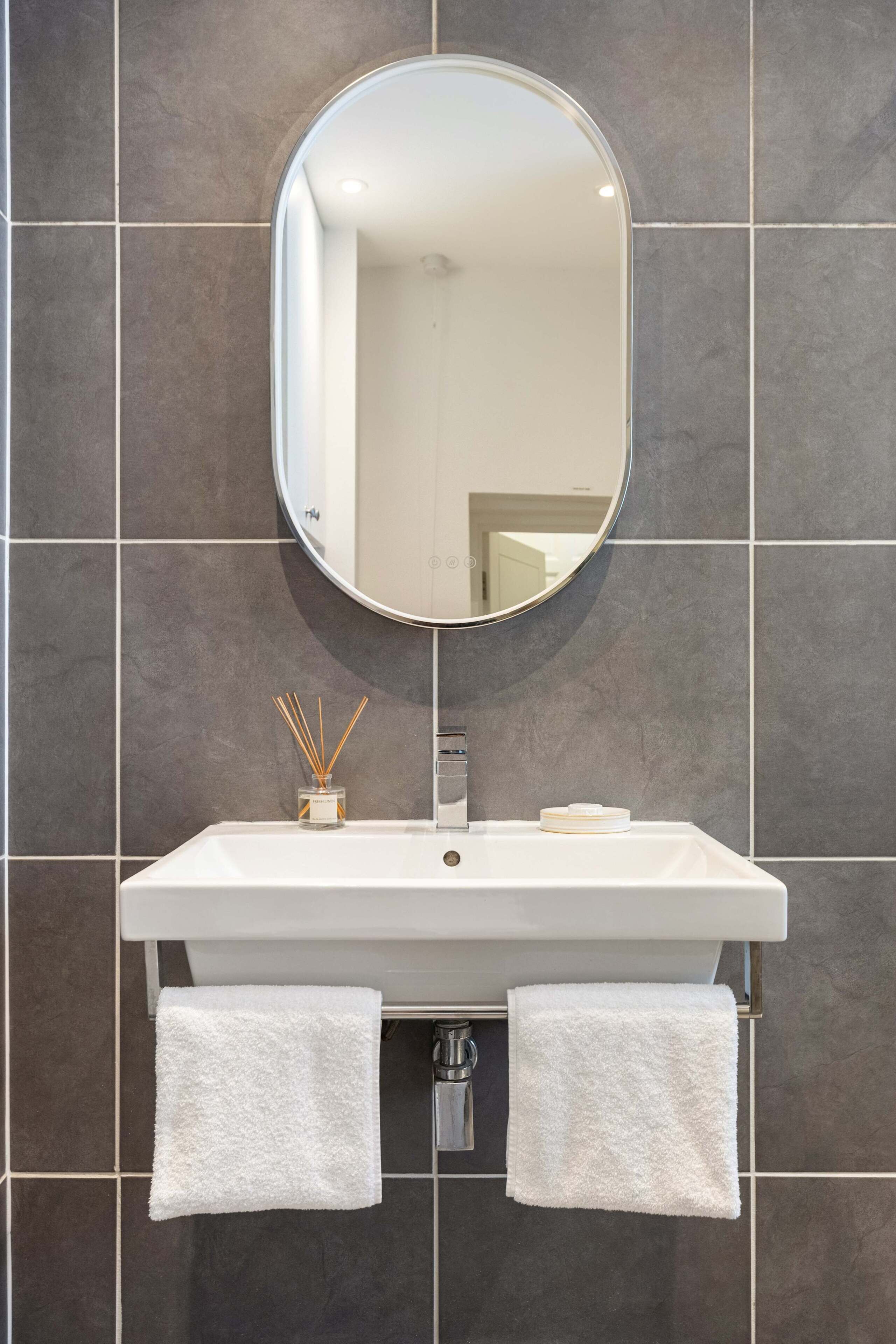 A bathroom with a white sink, a round mirror, and two towels hanging from the sink's side.