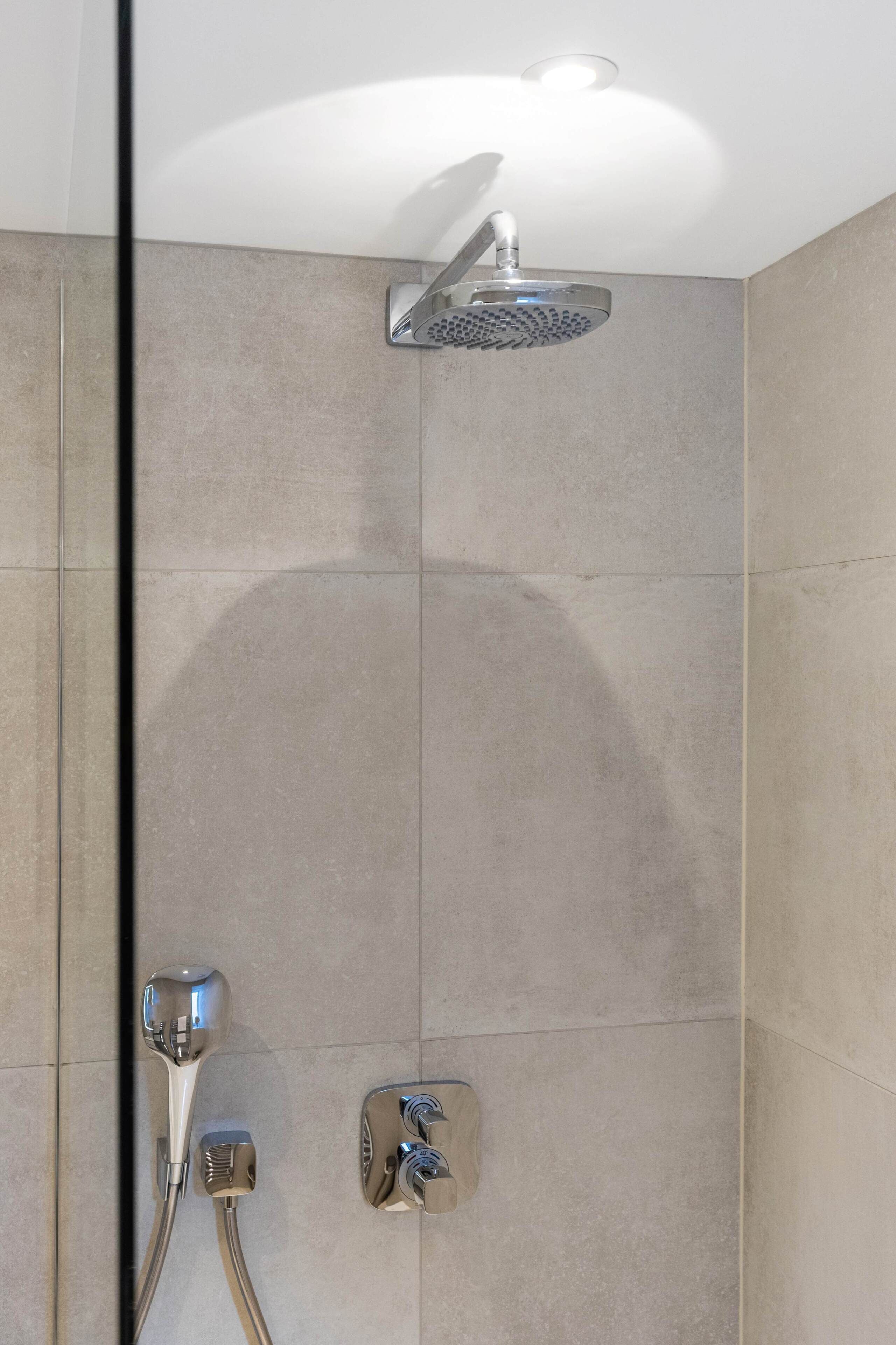 A modern shower with a handheld showerhead and a fixed overhead showerhead.