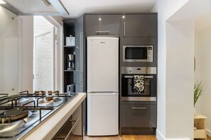Uma cozinha compacta com fogão a gás, geladeira branca, micro-ondas e forno embutido.