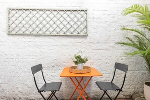 A small outdoor seating area with two chairs and a table, a potted plant, and a window with a lattice screen. - Primrose Hill 1BR Flat - Private Patio (Greater London)