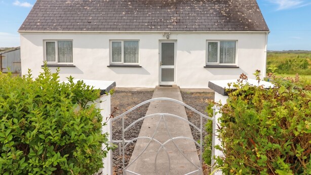 A white two-story house with a grey roof, a front door, and two windows on the ground floor. - Golf Club View (Doonbeg)