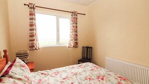 A bedroom with a bed, a chair, a lamp, and a window with curtains. - Golf Club View (Doonbeg)