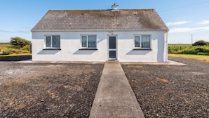 A white single-story house with a tiled roof, a front door, and two windows on the ground floor. - Golf Club View (Doonbeg)