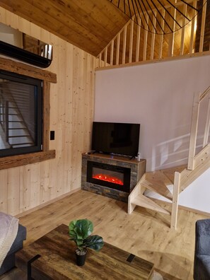 Een gezellige woonkamer met een open haard, een televisie en een houten trap.