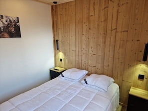 Ein Zimmer mit einer Holzwand, einem Bett mit weißer Bettwäsche, einem Nachttisch mit Lampe und einer Fernbedienung.