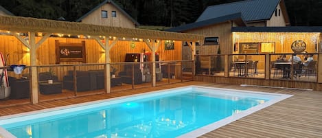 A pool area with a wooden deck, a covered seating area with string lights, and a building with a sign 'Luma Beach'.