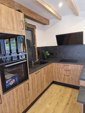 Eine moderne Küche mit Holzausstattung, einem Backofen, einer Spüle und einem an der Wand montierten Flachbildfernseher.