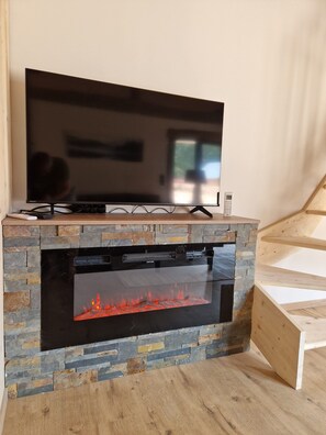 Ein Flachbildfernseher an einem Steinkamin mit Glastür, und eine Holztreppe zur Rechten.
