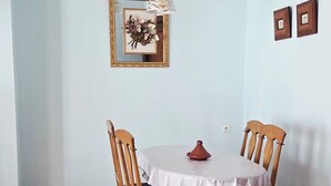 A dining area with a round table, four wooden chairs, a white tablecloth, a decorative vase, and a wall-mounted light fixture. - Coffee baba Chefchaouen (Chefchaouen)