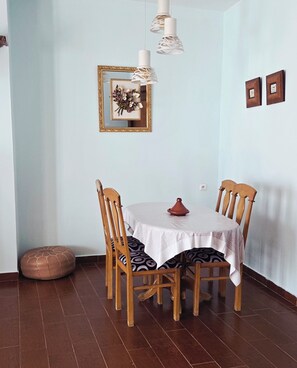 A dining area with a round table, four wooden chairs, a white tablecloth, a decorative vase, and a wall-mounted light fixture. - Coffee baba Chefchaouen (Chefchaouen)