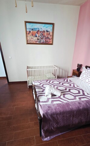A bedroom with a bed, a crib, a painting, and a nightstand. - Coffee baba Chefchaouen (Chefchaouen)