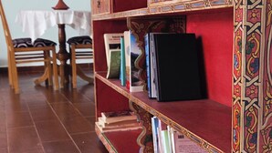 A bookshelf with books and decorative items, a wooden chair, and a table with a white cloth. - Coffee baba Chefchaouen (Chefchaouen)