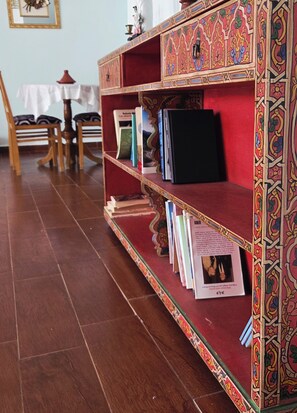 A bookshelf with books and decorative items, a wooden chair, and a table with a white cloth. - Coffee baba Chefchaouen (Chefchaouen)