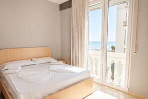 A hotel room with a bed, a nightstand, and a view of the sea through a glass door. - Illyrian Apartment 05 (Durrës)
