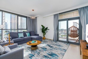 A modern living room with a sectional sofa, a coffee table, and a large window with a city view. - bnbme - Dubai Creek Residences - 2BR (Dubai)