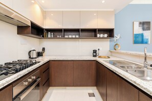 A modern kitchen with a gas stove, stainless steel appliances, and a built-in oven. - bnbme - Dubai Creek Residences - 2BR (Dubai)