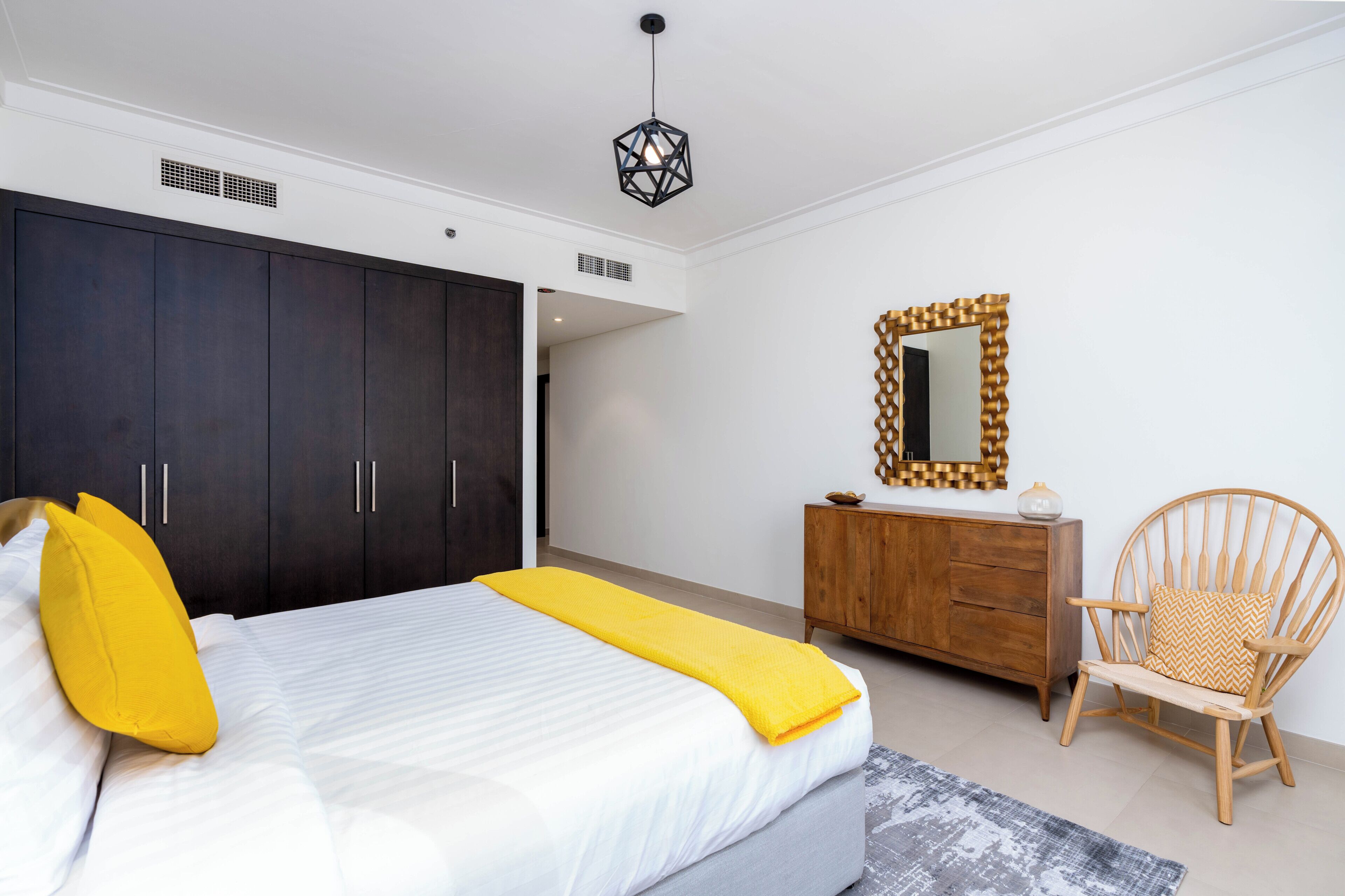 Quarto com cama, guarda-roupa, penteadeira, cadeira e luminária suspensa.