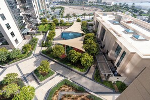 A modern building with a rooftop pool, surrounded by greenery and a covered seating area. - bnbme - Dubai Creek Residences - 2BR (Dubai)