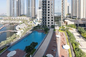 A high-rise residential building with a swimming pool, palm trees, and a marina. - bnbme - Dubai Creek Residences - 2BR (Dubai)