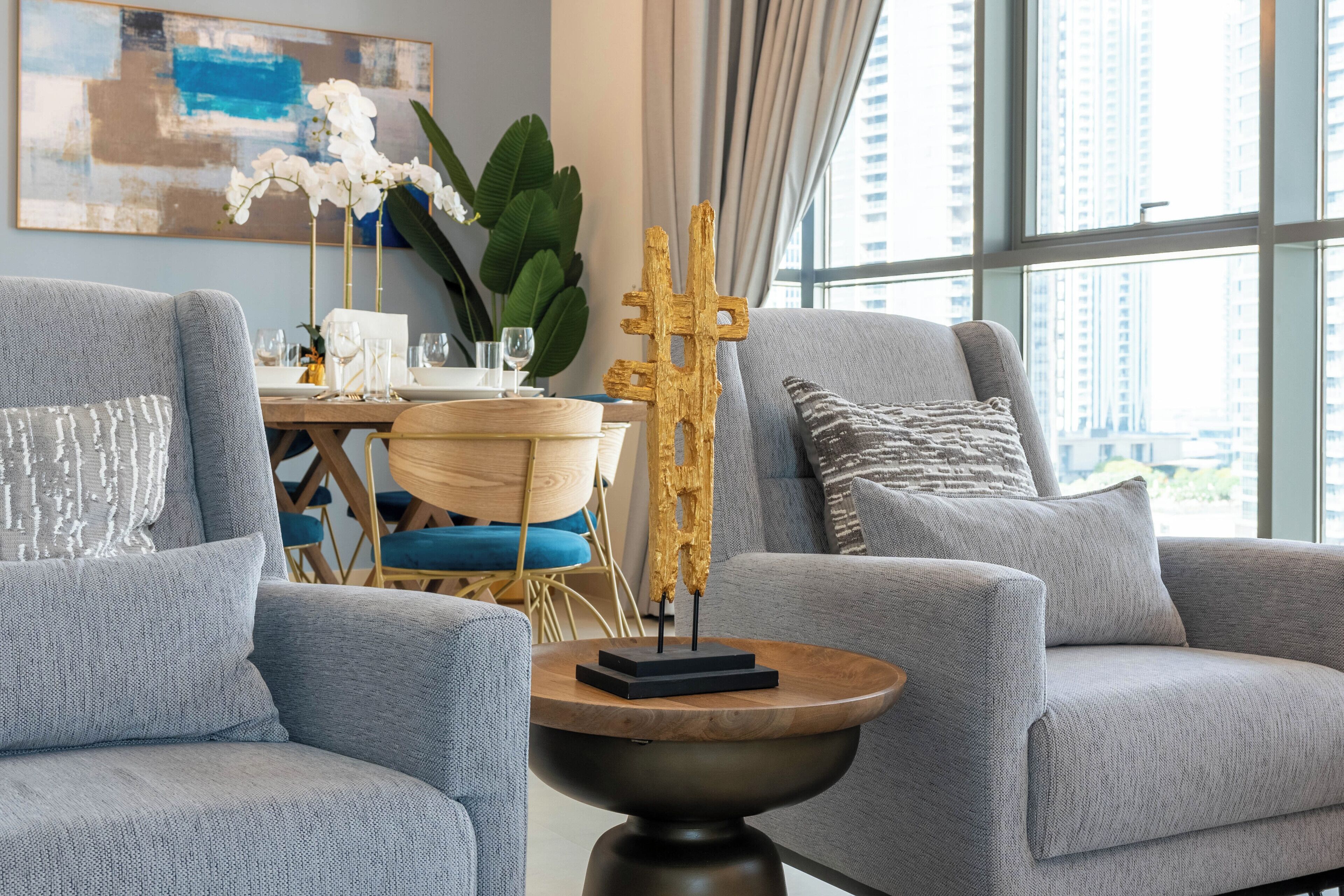 Ein modernes Wohnzimmer mit grauen Sofas, einem runden Holztisch und einer dekorativen, goldenen Skulptur.