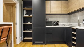 Uma cozinha compacta com armários pretos, máquina de café embutida e piso de madeira.