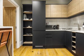 A compact kitchen with black cabinetry, a built-in coffee machine, and a wooden floor. - Central Russell Square Studio Retreat (Greater London)