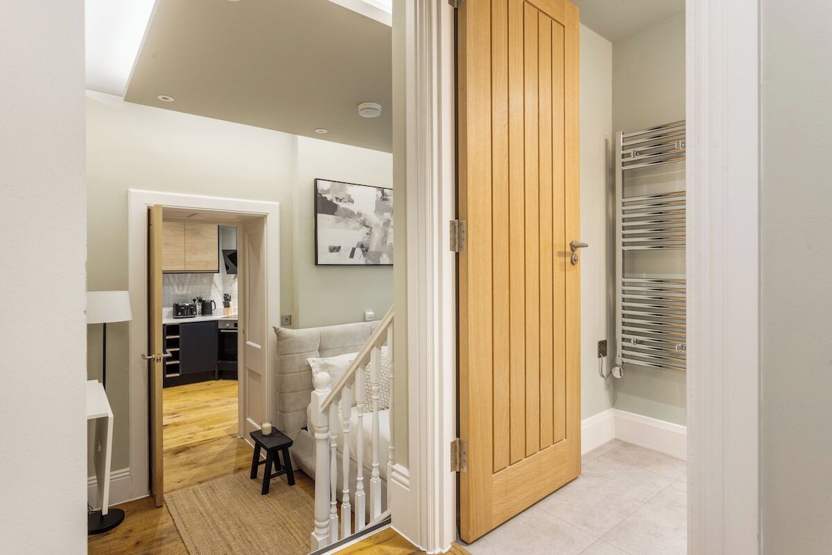 A hallway with a wooden door, a staircase, and a kitchen area visible through an open door.