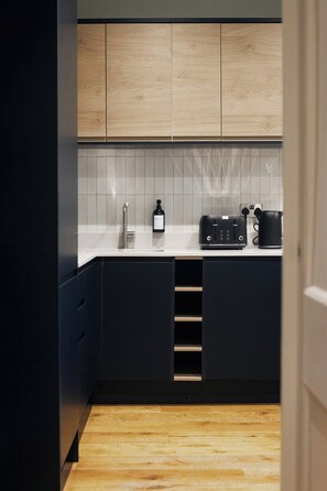 A modern kitchen with dark cabinets, a tiled backsplash, and a countertop with a coffee maker and a bottle. - Central Russell Square Studio Retreat (Greater London)