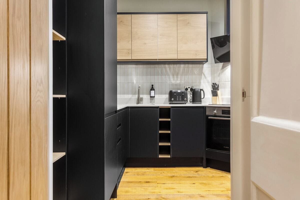 Cocina compacta con alacenas negras, encimera de madera y horno empotrado.