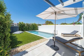 Ein modernes Pool-Areal im Freien mit blauem Himmel, einem Schwimmbecken, Liegestühlen und einem großen Sonnenschirm.