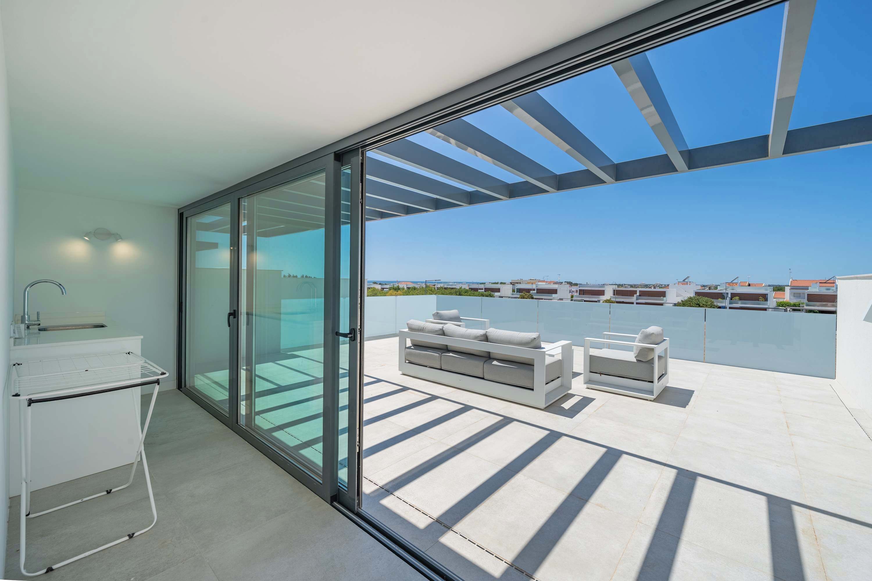 A modern balcony with a glass door leading to a pool, a white sofa, and a small table with a lamp.