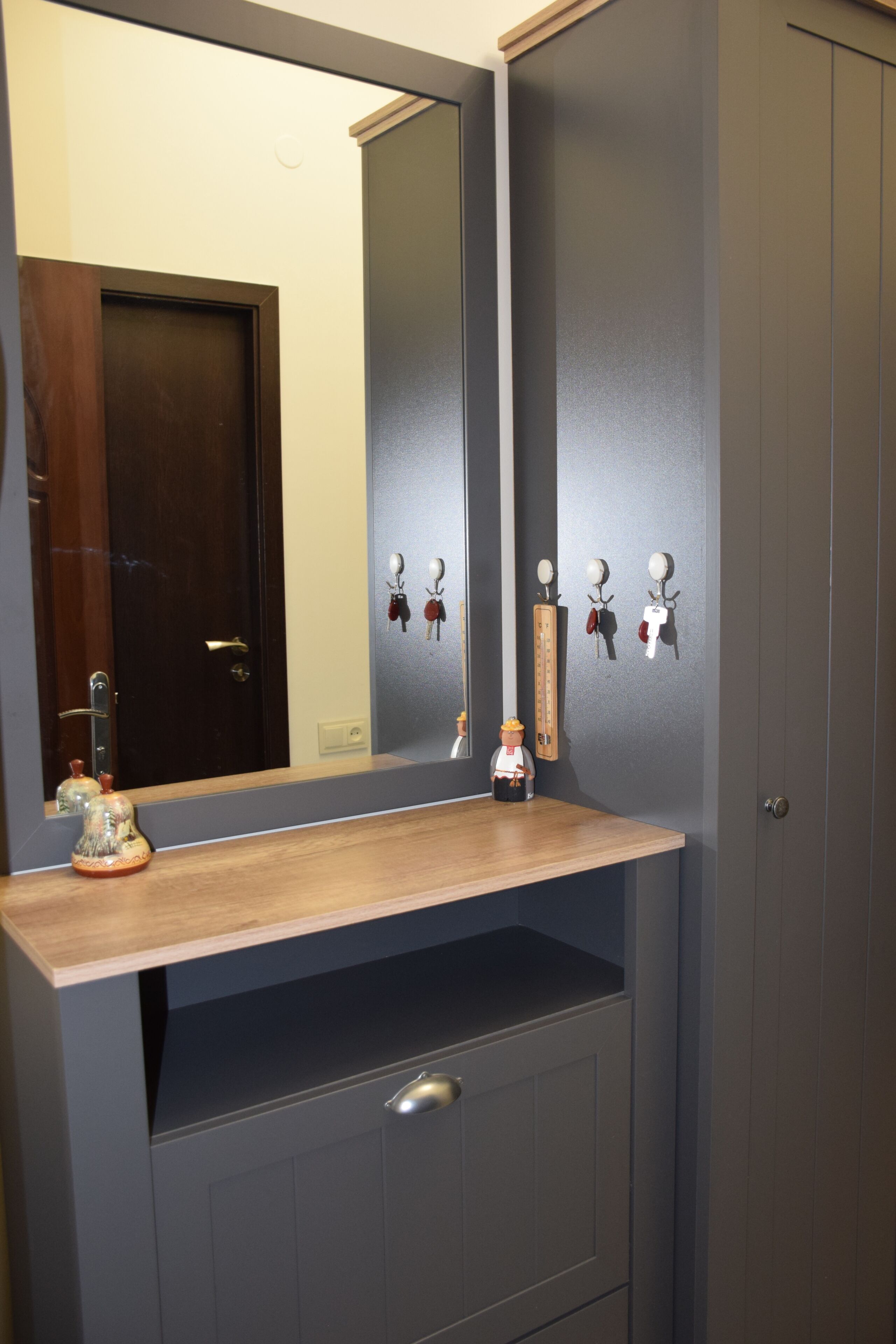 A bathroom with a wooden vanity, a mirror, and a wall-mounted towel rack with keys and a thermometer.