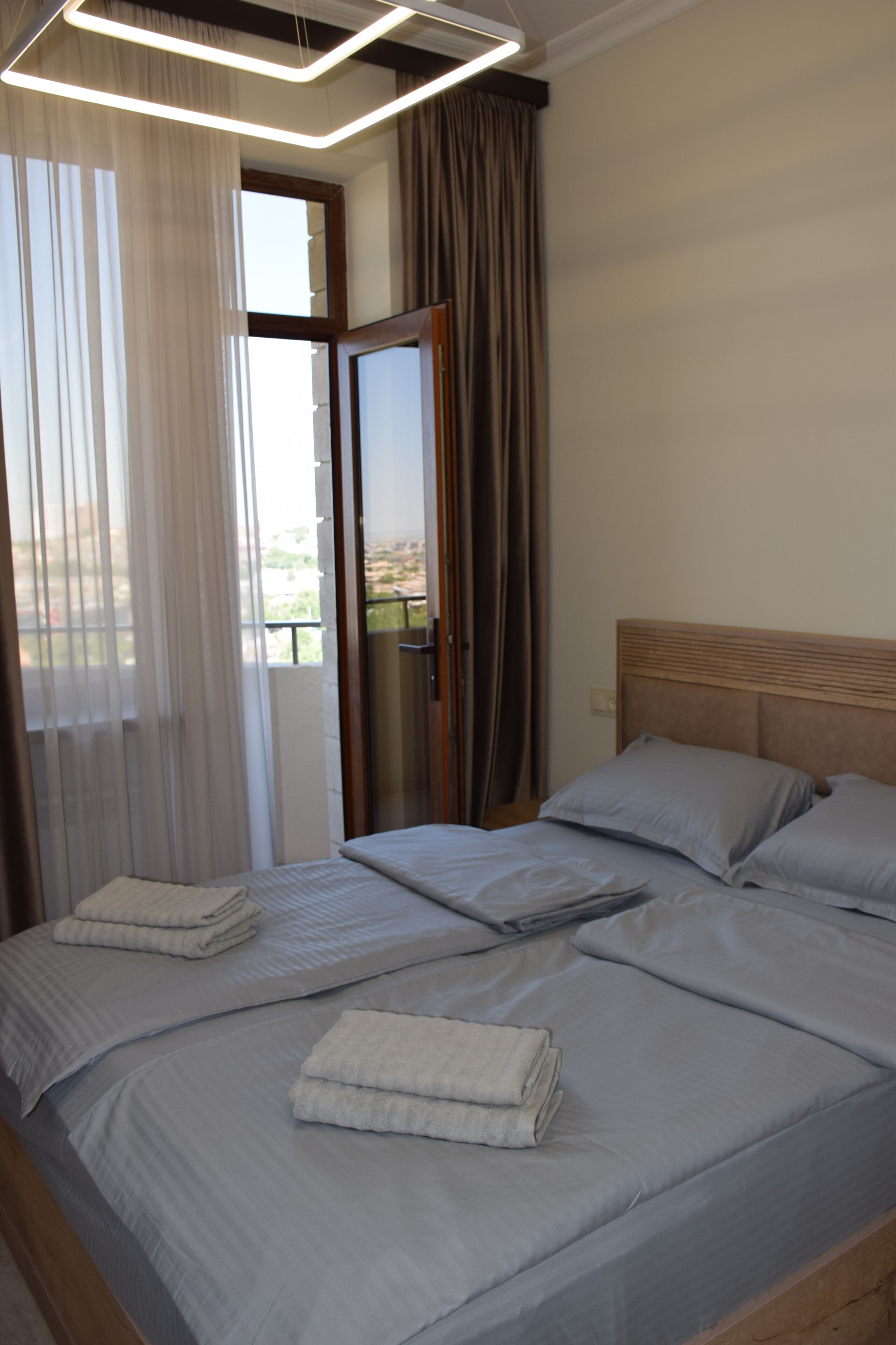 A hotel room with a bed, a view through the window, and a door.