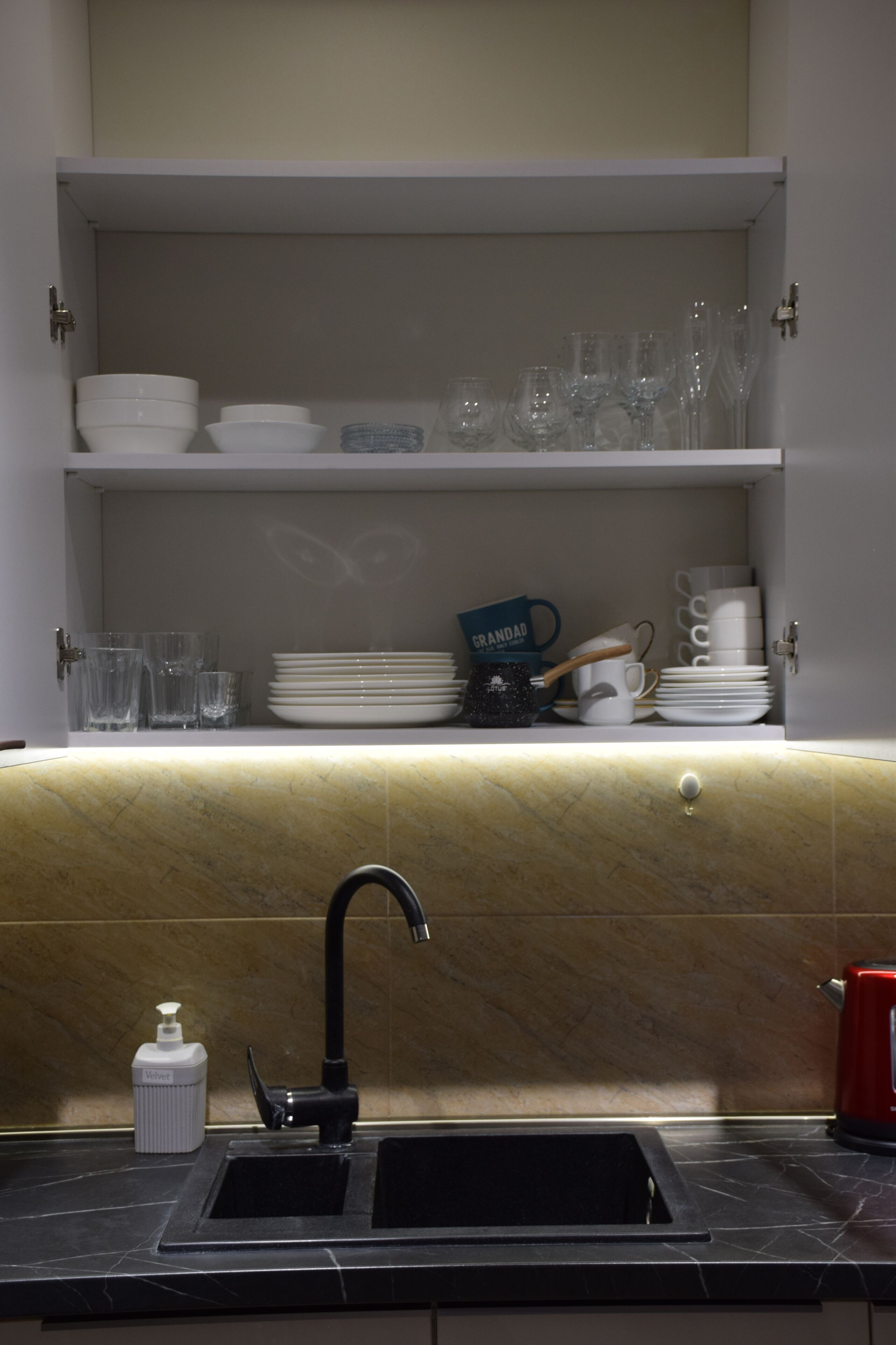 A kitchen with a black sink, a soap dispenser, and a coffee machine.