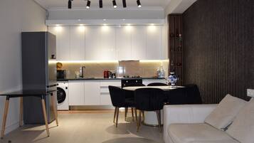 A modern kitchen with white cabinets, a dining area with a black table and chairs, and a sofa with cushions.