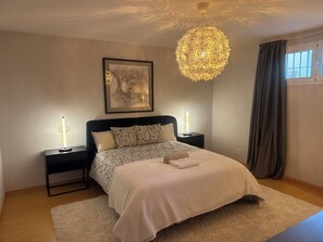 A bedroom with a bed, two bedside tables, a hanging light fixture, a framed artwork, and a window with curtains. - Villa Elysian, Amazing 5 BR house with AC and private pool 100m from golf club. (Benahavís)