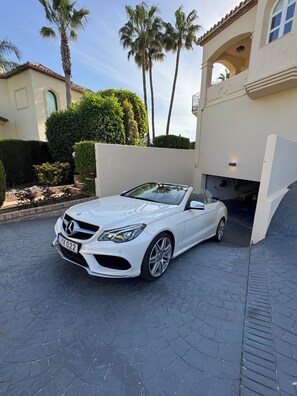 A white convertible car parked in front of a house with a paved driveway and palm trees. - Villa Elysian, Amazing 5 BR house with AC and private pool 100m from golf club. (Benahavís)