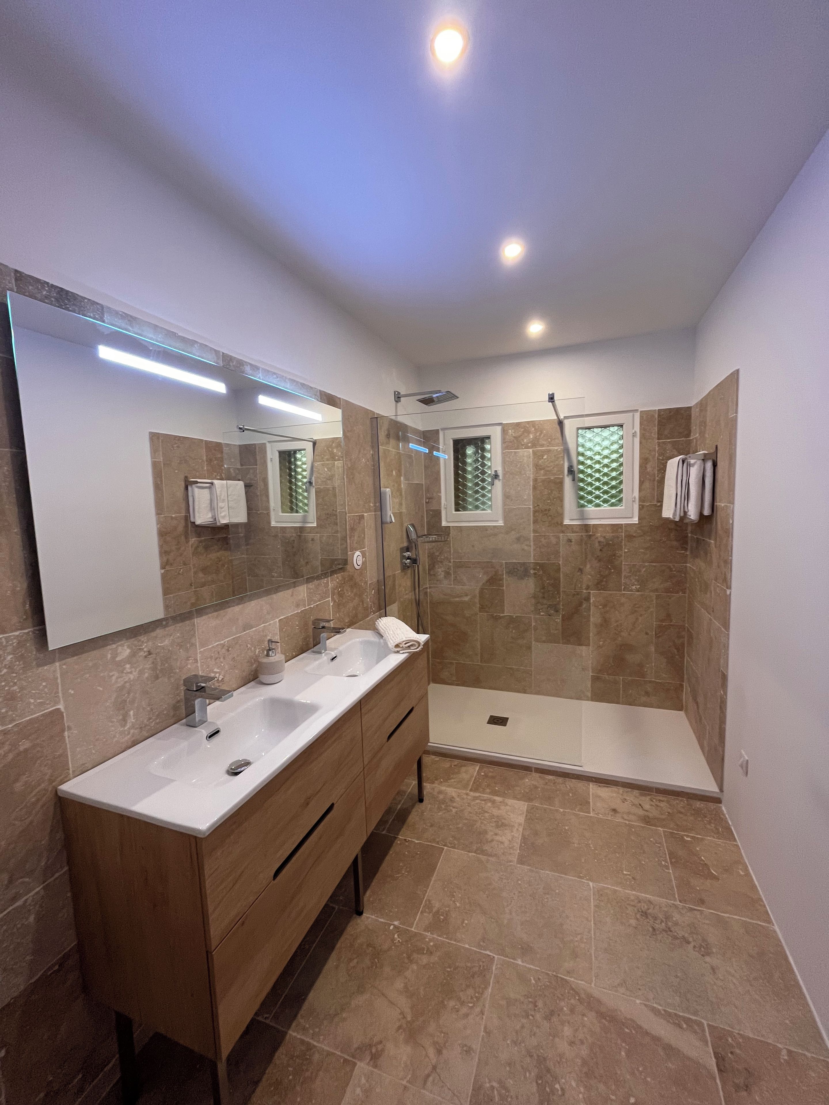 Een moderne badkamer met een wastafelmeubel met dubbele wastafel, een douchecabine van glas en een inloopdouche.