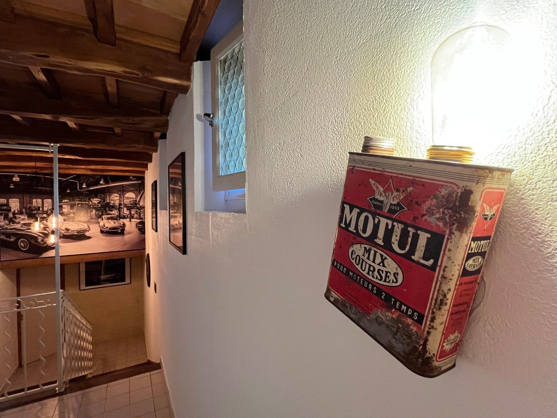 Un contenedor mural etiquetado 'MOTUL' con diseño vintage, situado en una habitación con vigas de madera y una escalera visible.